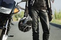 A woman biker holds a protective helmet in her hand, standing next to a motorcycle. Close-up