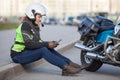 Woman biker trying to find road with sat nav while sitting on roadside near motorcycle Royalty Free Stock Photo