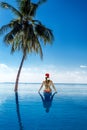 Woman in bikini and Santa hat sitting on paradise beach, enjoying winter holidays and celebrating Christmas at tropical Royalty Free Stock Photo