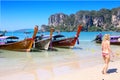 A woman in a bikini walks along the beach past long tailed boats