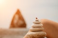 Woman bilds stones pyramid on seashore on a sunny day on the blue sea background. Happy holidays. Pebble beach, calm sea