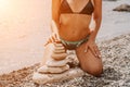 Woman bilds stones pyramid on seashore on a sunny day on the blue sea background. Happy holidays. Pebble beach, calm sea