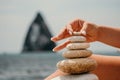 Woman bilds stones pyramid on seashore on a sunny day on the blue sea background. Happy holidays. Pebble beach, calm sea Royalty Free Stock Photo