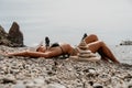 Woman bilds stones pyramid on seashore on a sunny day on the blue sea background. Happy holidays. Pebble beach, calm sea