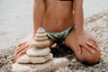 Woman bilds stones pyramid on seashore on a sunny day on the blue sea background. Happy holidays. Pebble beach, calm sea Royalty Free Stock Photo