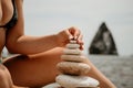 Woman bilds stones pyramid on seashore on a sunny day on the blue sea background. Happy holidays. Pebble beach, calm sea