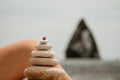 Woman bilds stones pyramid on seashore on a sunny day on the blue sea background. Happy holidays. Pebble beach, calm sea Royalty Free Stock Photo