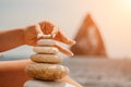 Woman bilds stones pyramid on seashore on a sunny day on the blue sea background. Happy holidays. Pebble beach, calm sea