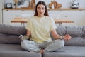 Woman with a bionic prosthetic arm sits at home on a sofa in a lotus position and meditates