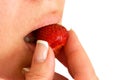 Woman bites and eats strawberry closeup image. Part of face with mouth and lips. Red berry is in fingers with clear nails. Royalty Free Stock Photo