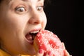 A woman bites a large red donut, a black background, a place for text. Gluttony, overeating and sugar addict.