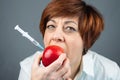 Woman bites a red apple. GMO injection. Close-up. Genetically modified foods
