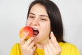 A woman bites a red apple while holding a multivitamin pill in her hand