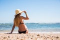 Woman in black bikini resting on the beach in straw hat near sea