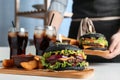 Woman with black burger, fries and drinks served on table