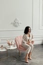 Woman with curly hair sits in a pink armchair next to a bouquet of flowers