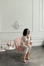 Woman with curly hair sits in a pink armchair next to a bouquet of flowers