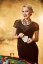 A woman in a black dress with cards in her hands is standing near the poker table