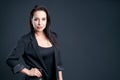 A woman in black jacket and black shirt stands in front dark background