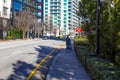 A woman in a black jacket and jeans pushing a stroller along the sidewalk surrounded by buildings, bare winter trees