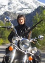 A woman in a black leather biker jacket with a carbine rifle on a chopper motorcycle in Greece on a road in the forest in the moun Royalty Free Stock Photo