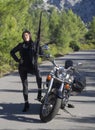 A woman in a black leather biker jacket with a carbine rifle on a chopper motorcycle in Greece on a road in the forest in the moun Royalty Free Stock Photo