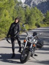 A woman in a black leather biker jacket with a carbine rifle on a chopper motorcycle in Greece on a road in the forest in the moun Royalty Free Stock Photo