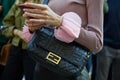 Woman with black leather Fendi bag with golden logo and pink cuffs before Bottega Veneta