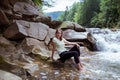 Woman in black leggings is sitting at stone near at Splashing Waterfall