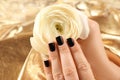 Woman with black manicure holding beautiful flower on golden background. Nail polish trends