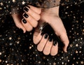 Woman with black manicure holding nail polish bottle over dark fabric