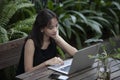 Woman in black outfit working with her laptop in a garden surrounded by greeneries