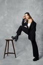 Woman in black pantsuit put leg in ankle boot with rough sole on tall stool