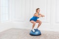 Woman in black shorts and blue top working in gym doing exersice in bosu balance trainer, squats on fitness ball, holding balance Royalty Free Stock Photo