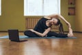 Woman in black sportswear does yoga, performs online exercise Parivritta Janu Shirshasana, looks into a laptop