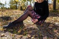 Woman in black sweater and sirt with flowrs sitting in autumn forest. Female hands with red manicure hugging legs