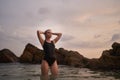 Woman in black swimsuit enjoys serene sea dip at dusk. Wellness, nature immersion scene. Female relaxes in ocean water Royalty Free Stock Photo