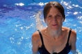 Woman in black swimsuit exiting pool on sunny day with water droplets falling from her hair Royalty Free Stock Photo