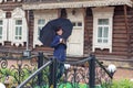 A woman with a black umbrella on the background of an old wooden building looks