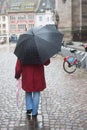 Woman with black umbrella and red coat walking in cobbles street Royalty Free Stock Photo