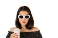 Woman in a black and white dress with polka dots and white sunglasses holding a glass of coffee. Royalty Free Stock Photo
