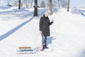 A woman in a black winter jacket with sledges in a snow-covered park or forest