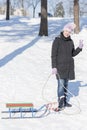 A woman in a black winter jacket with sledges in a snow-covered park or forest. vertical photo