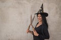 Woman in black witch suit and hat, with huge pruning shears in hands very smiling with gray cement background, celebrating