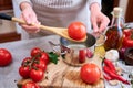 woman blanching a tomato holding over pan with hot water for further peeling