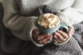 Woman with blanket warming her hands in mug of hot drink with whipped cream