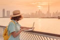 Blogger or copywriter or student works and studies using a laptop and admires the colorful sunset over Dubai Creek with a