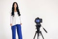 A woman blogger records a video in a white photo studio on a professional video camera on a tripod Royalty Free Stock Photo