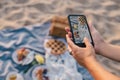 Woman blogger shooting picnic at beach on her smart phone.