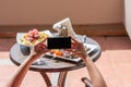 Woman blogger taking a picture on mobile phone plate with lamb potato and salad on the table outside on the balcony. Top view.